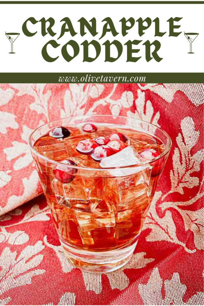 CranApple Codder in a rocks glass with ice and fresh cranberries garnish. Red and tan clothe background.