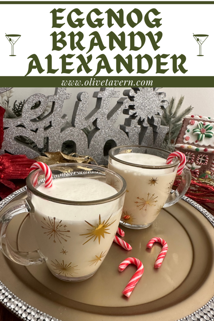 Two holiday mugs of cocktail with candy cane garnishes. Background: Glittery let it snow sign and gingerbread house.