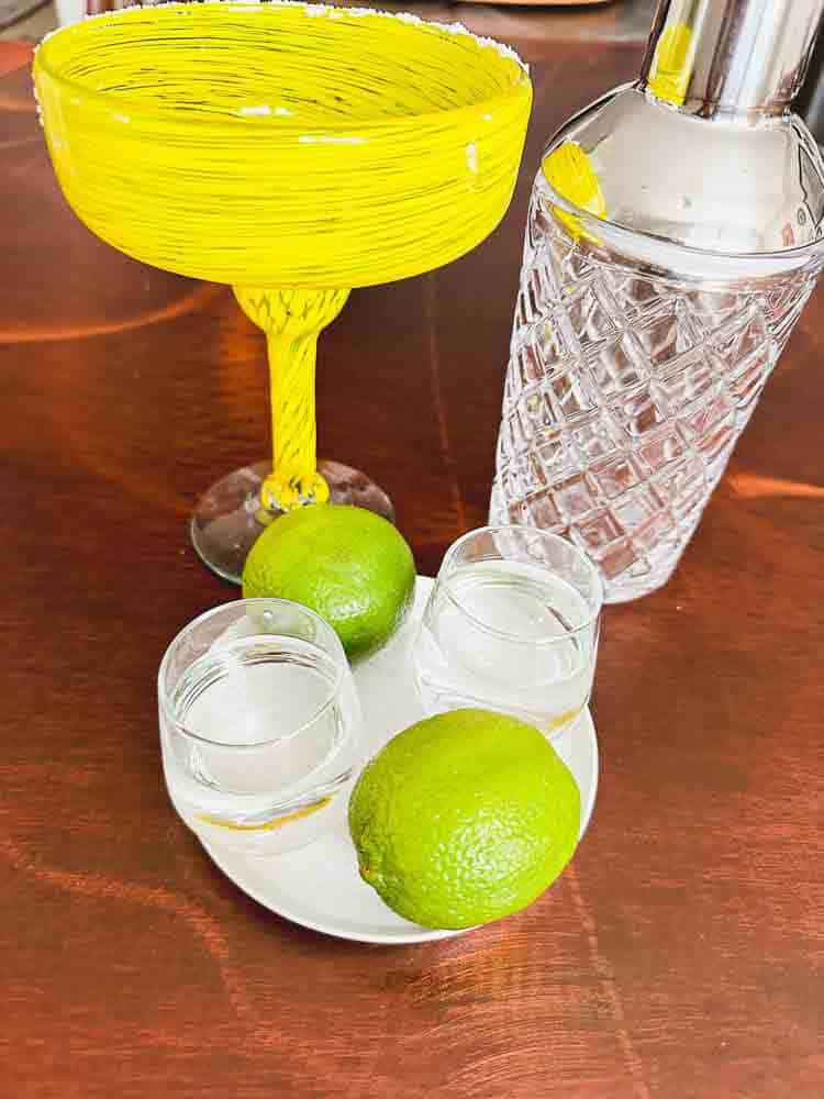 Margarita glass, Glass Shaker, Limes, Glasses with Tequila and Triple Sec, Plate with salt.