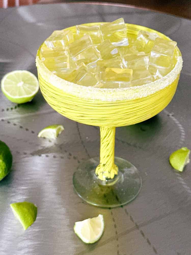 Margarita cocktail in a yellow margarita glass with slices of limes in the background.