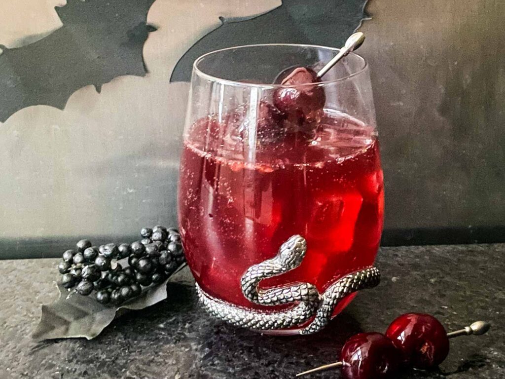 A stemless glass filled with Bloody Heart Halloween Cocktail and a pick of brandied cherries.