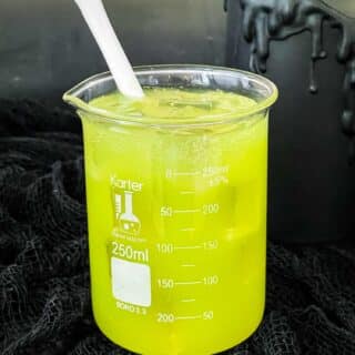 Bright green vodka Toxic Waste Cocktail in a glass beaker with a white bone stir stick on a black cloth