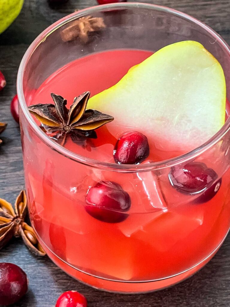 Closer view of Autumn Harvest Cocktail in a glass with floating cranberries and a pear slice