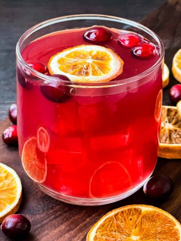 A glass of Cranberry Bog Cocktail with a floating dried orange and cranberries