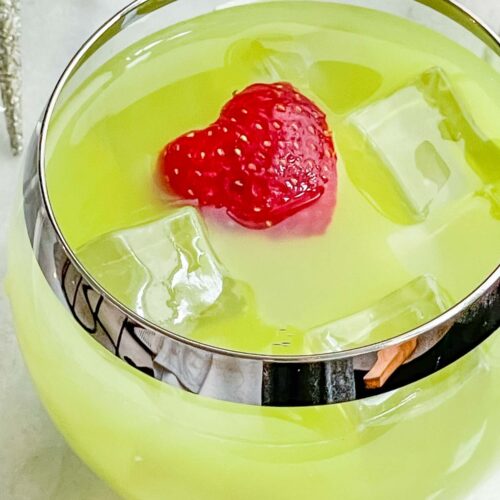 Top view of a green Grinch Cocktail in a round glass with a strawberry heart
