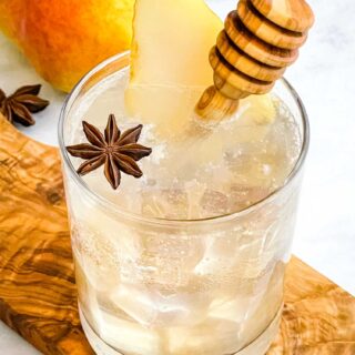 A glass of Honey Pear Collins garnished with a pear slice and honey stirrer, sitting on a wood board