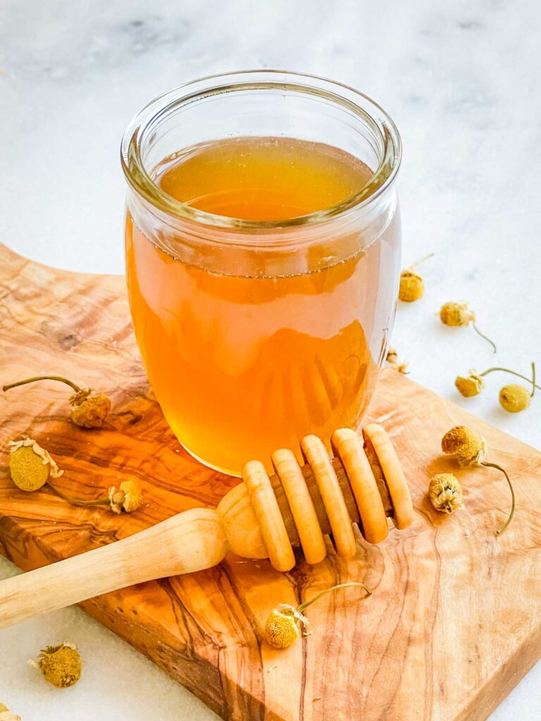 Honey Simple Syrup in a glass jar on a wood board with dried flowers and a honey dipper