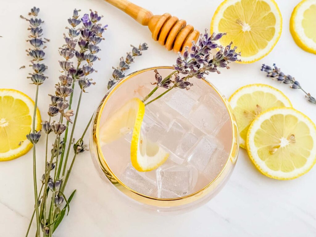 Top view down of a Lavender Field Mocktail surrounded by lavender, lemons, and a honey stirrer