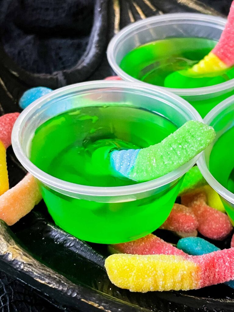 A close up view of one green Rotten Apple Halloween Jello Shot with a gummy worm coming out of it