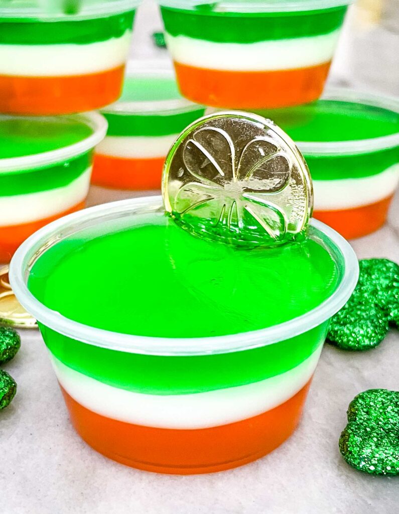 A close view of St Patrick's Day Jello Shots in plastic cups with a gold coin sticking out of the one in front