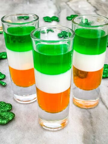 Double tall shot glasses layered with green, white, and orange St Patrick's Day Jello Shots on a counter