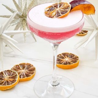 A pink Sugar Plum Fairy Cocktail (Plum Sour) in a glass coupe on a white counter with dried lemons