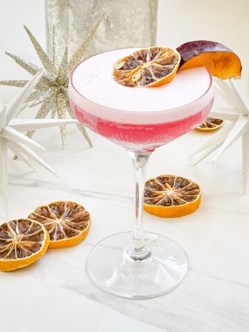A pink Sugar Plum Fairy Cocktail (Plum Sour) in a glass coupe on a white counter with dried lemons