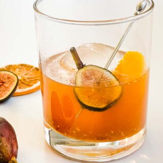 Fig Old Fashioned in a glass with ice on a white counter with a fresh fig inside.