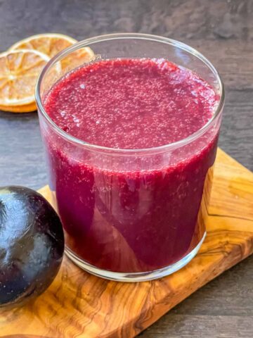 A glass full of Plum Juice on a piece of wood board.