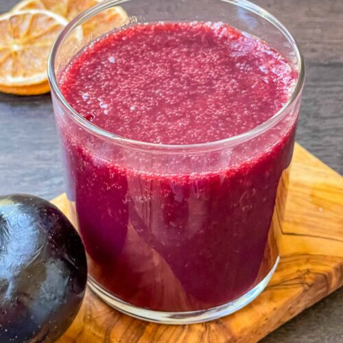 A glass full of Plum Juice on a piece of wood board.