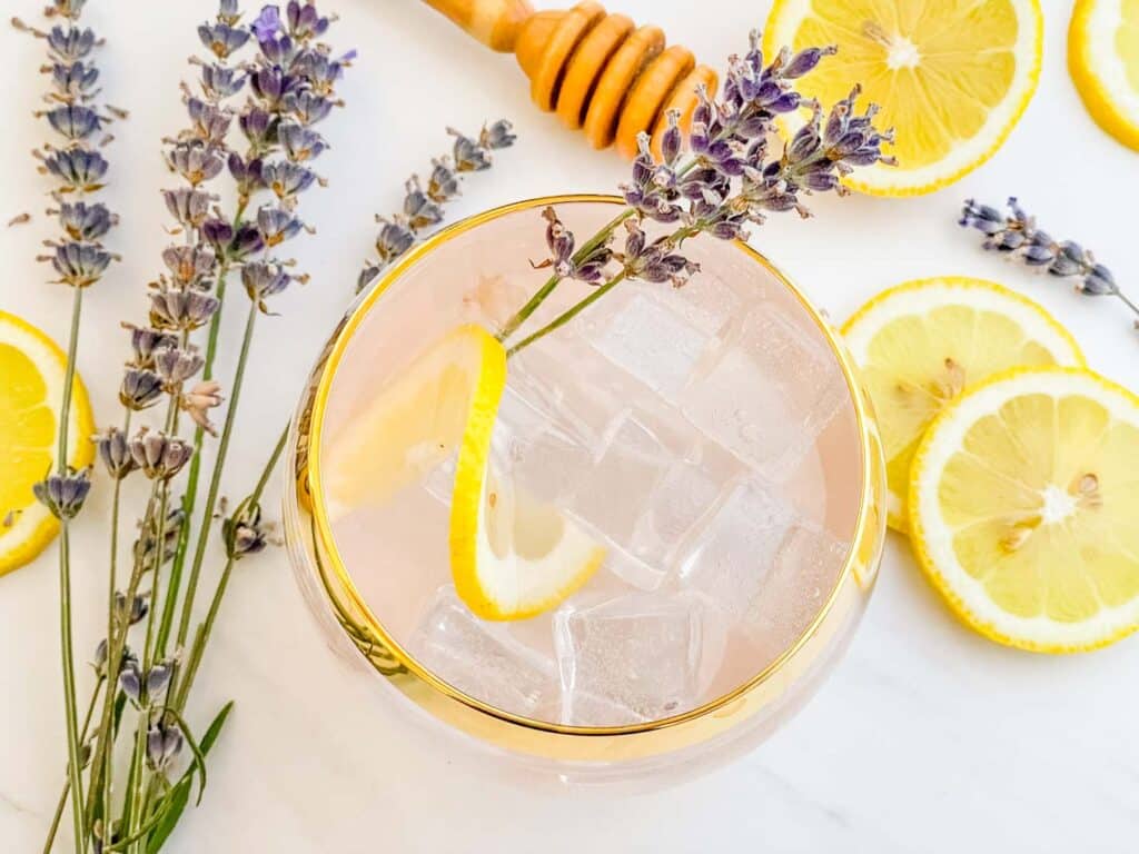 Looking down on a glass of Lavender Garden Cocktail on a counter with lemon and lavender around it.