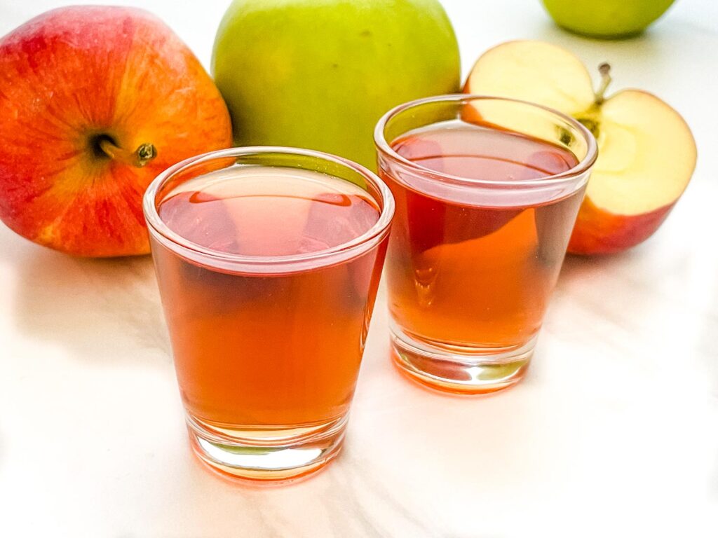 Two Washington Apple Shots in front of apples on a counter.