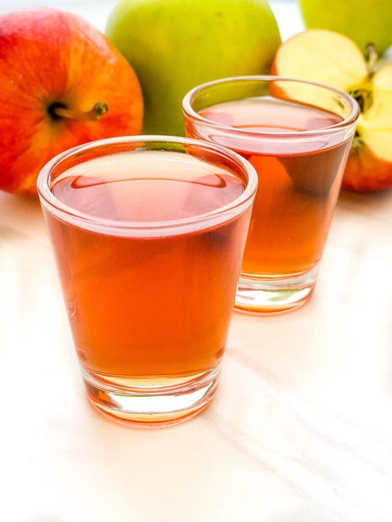 Closer view of two Washington Apple Shots on a counter with apples behind them.