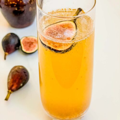 A stemless glass of Fig Mimosa cocktail on a counter with fresh figs.