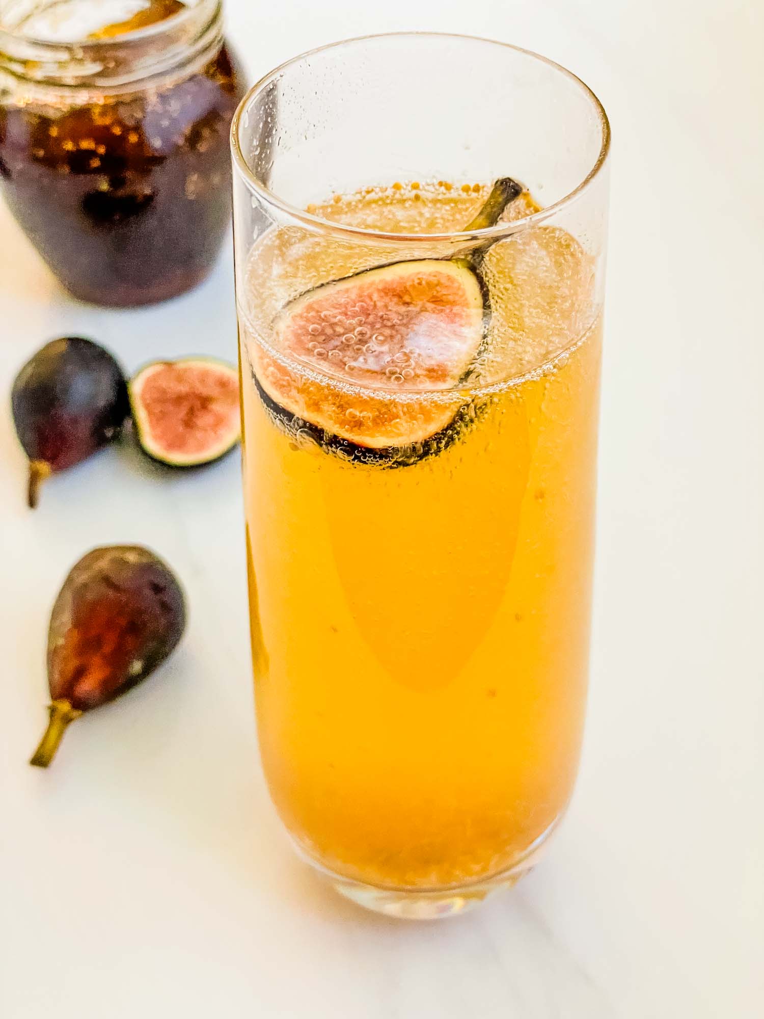 A stemless glass of Fig Mimosa cocktail on a counter with fresh figs.