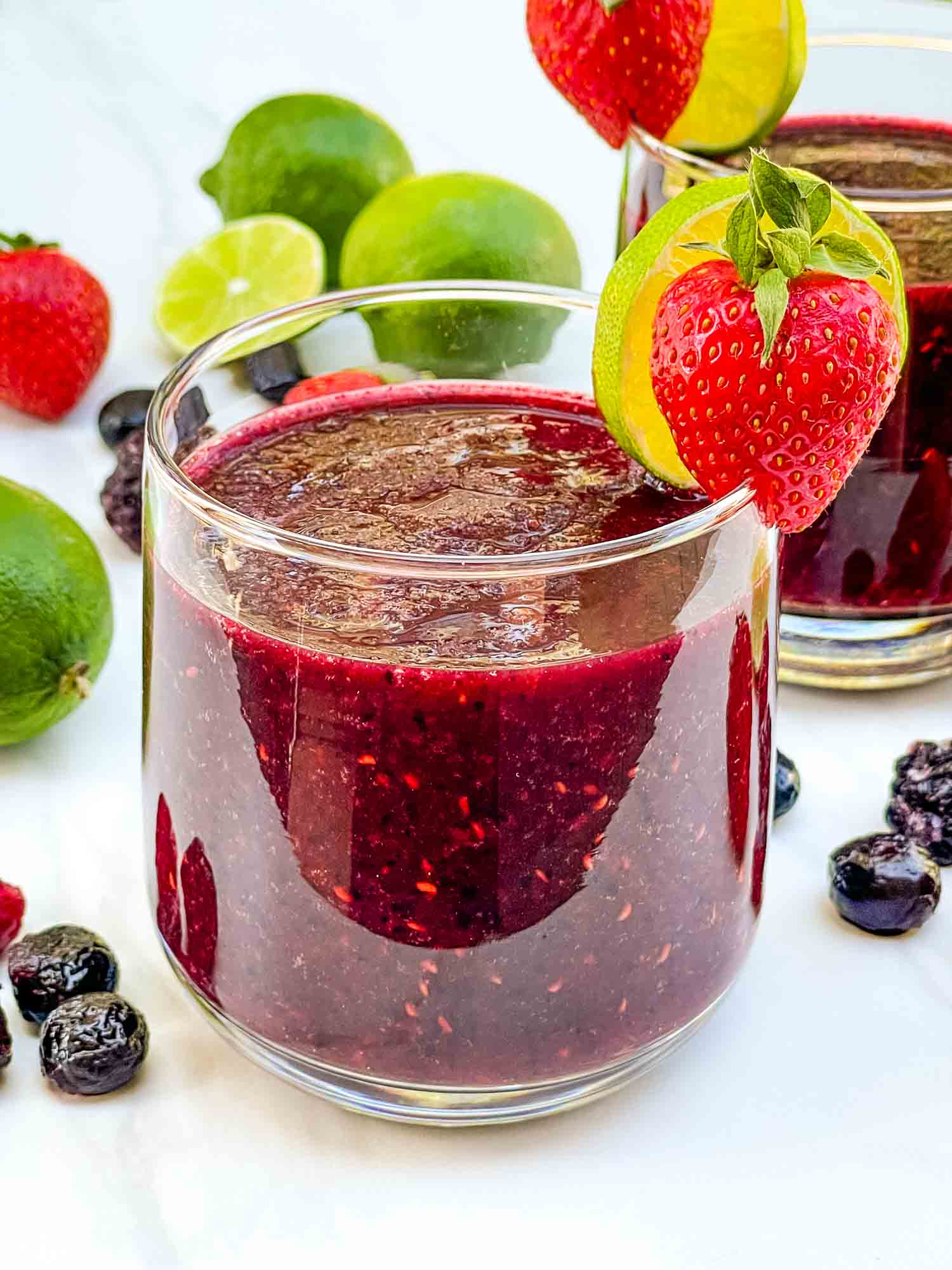 A close view of a purple red Frozen Mixed Berry Margarita cocktail with fruit garnish.