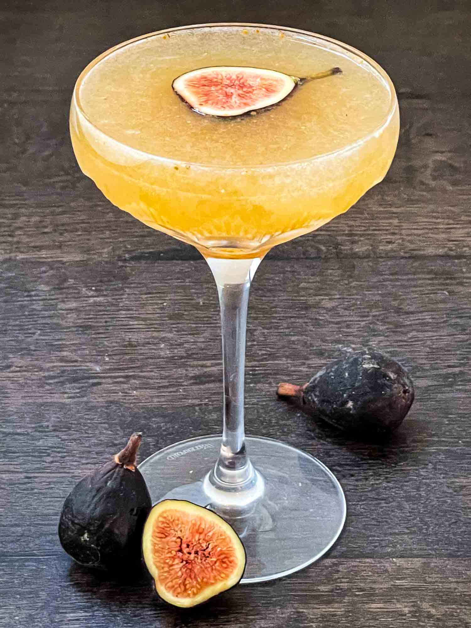 A coupe glass full of Fig Prosecco Cocktail with fresh figs around it.