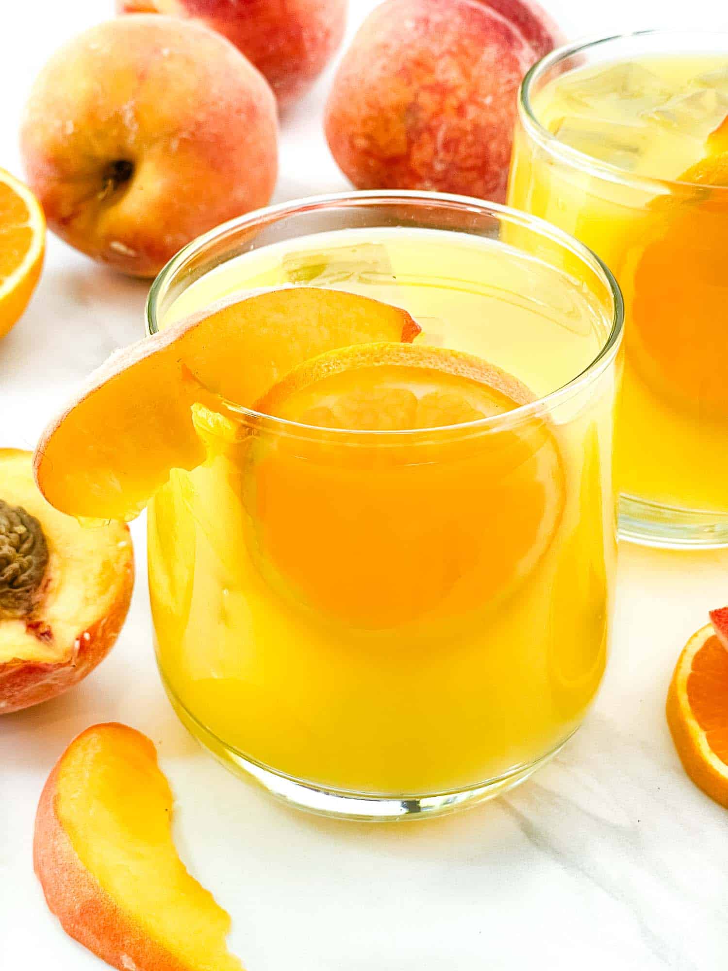 A Fuzzy Navel Cocktail garnished with a peach and orange slice.